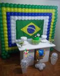 Painel de balões nas cores da copa (verde, amarelo, azul e branco); bolo provençal; mesa provençal; kachepot com bola e arranjo com fuleco